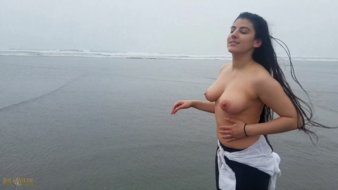 Behind the scenes of a wet and revealing public beach shoot with a stunning busty Latina