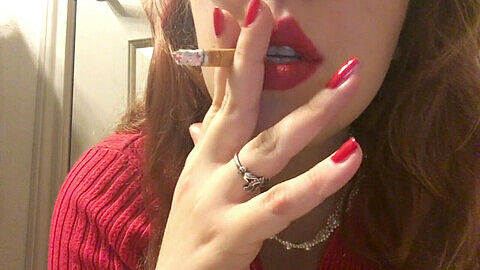 Sexy rothaarige Teenagerin raucht und zeigt roten Pullover, Lippenstift und Nägel